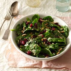 a white bowl filled with spinach and cranberries on top of a table