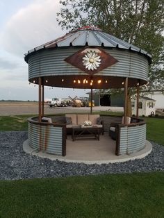 an outdoor gazebo with seating and lights on the top is shown in front of a field