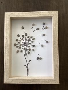 a shadow box with a dandelion in it on a wooden table next to a wall