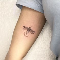 a small tattoo on the arm of a woman with a bee and sunburst