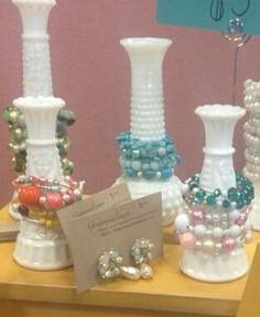 several white vases with different colored beads on them are sitting on a table in front of a pink wall