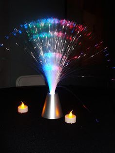 three lit candles sitting on top of a table next to a vase with colorful lights in it