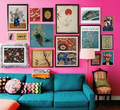 a blue couch sitting in front of a pink wall with pictures on the wall above it