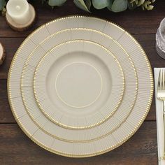 a white plate with gold trim sits on a wooden table next to silverware and greenery