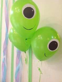 two green balloons with googly eyes hanging on a wall