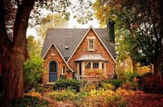 a red brick house surrounded by trees and flowers in the fall season with leaves on the ground