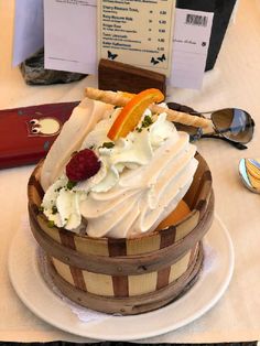 a cake with white frosting and fruit in a basket on a table next to spoons