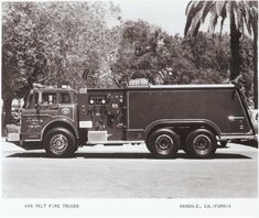 an old black and white photo of a fire truck parked in front of a palm tree