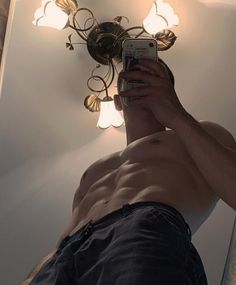 a shirtless man taking a selfie in front of a mirror with his cell phone