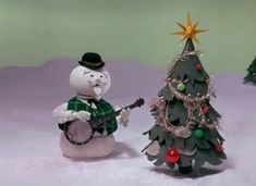 there is a snowman playing the guitar next to a small christmas tree with a star on top