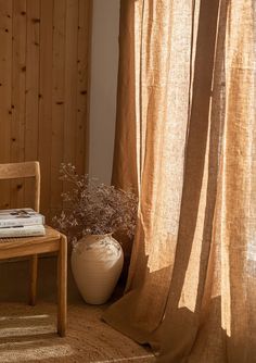 a wooden chair sitting next to a window covered in sheer curtains and a potted plant