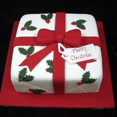 a christmas present cake with holly and red ribbon on the top is sitting on a table