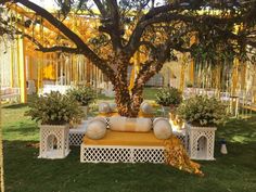 an outdoor seating area is decorated with yellow and white pillows, potted plants, and trees