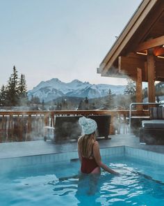 a woman in a red swimsuit is sitting in the hot tub with mountains in the background