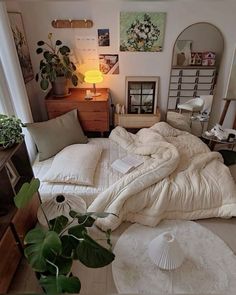 a bed with white sheets and pillows on top of it in a room filled with plants