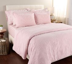 a bed with pink comforters and pillows in a white room next to a window