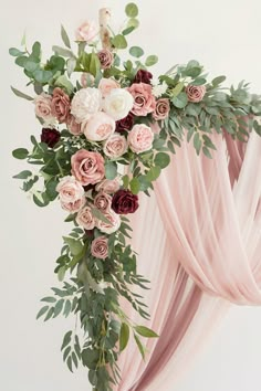 an arrangement of flowers and greenery on a pink drape