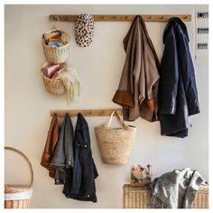 several coats hanging on a coat rack with baskets and blankets next to it in front of a white wall