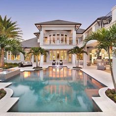 a large house with a swimming pool and palm trees in front of the house at dusk