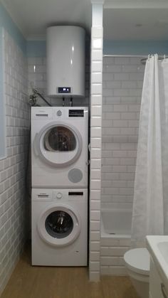 a washer and dryer in a bathroom next to a shower stall with white tiles on the walls