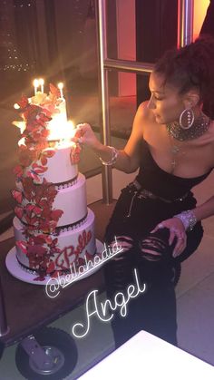 a woman sitting in front of a white cake with red flowers and candles on it