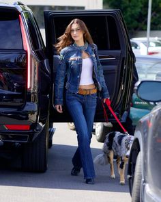 the woman is walking her dog down the street while wearing jeans and a jean jacket