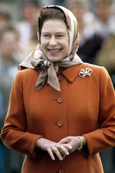 a woman in an orange coat smiles at the camera while wearing a headscarf