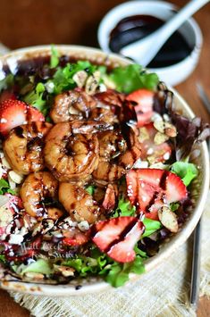 a salad with strawberries, nuts and dressing in it on a wooden table next to silverware