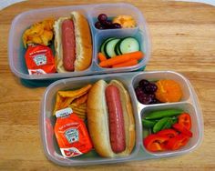 two plastic containers filled with hot dogs and veggies on top of a wooden table