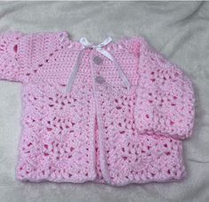 a pink crocheted sweater laying on top of a white bed sheet with a bow