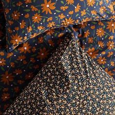 an orange flowered pillow is laying on top of a blue and green floral patterned bed sheet