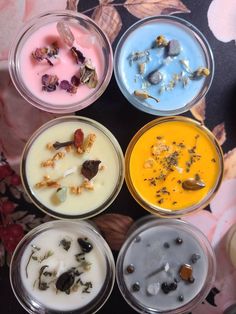 four different colored candles are in small glass containers with dried flowers on them, and one is empty