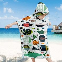 a woman standing on top of a sandy beach under a towel covered in cartoon fish