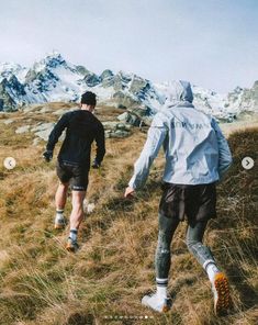 two men are running up a hill in the mountains