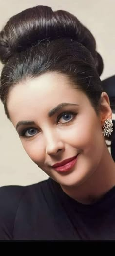 a woman with dark hair and blue eyes smiles at the camera while wearing an updo