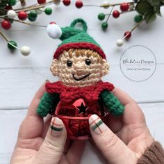 a hand holding a small crocheted christmas ornament in the shape of a smiling elf