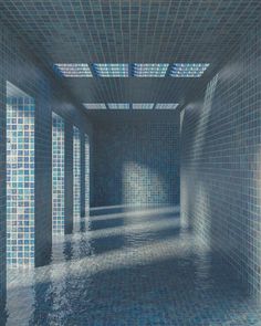 an empty room with blue tile walls and water in the floor is lit by sunlight coming through the window