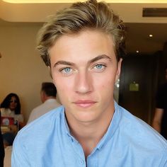 a young man in a blue shirt is staring at the camera with people behind him