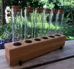 four empty glass bottles sitting on top of a wooden stand in front of some flowers