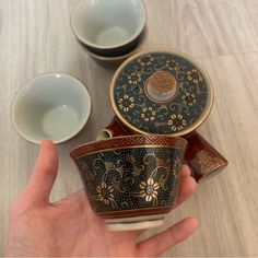 a hand is holding three tea cups and saucers on a wooden table with other dishes