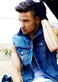 a young man sitting in the back of a car wearing a denim vest and jeans