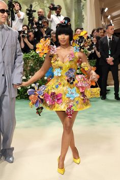 a woman in a yellow dress walking down a runway next to a man in a gray suit