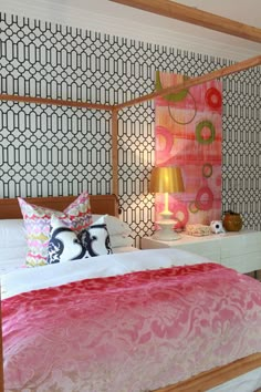 a bed with pink and white comforter next to a wallpapered headboard