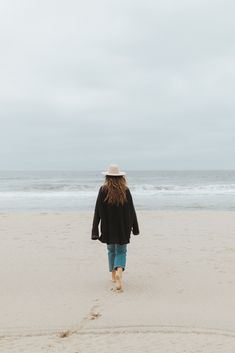 a woman walking on the beach with her back to the camera