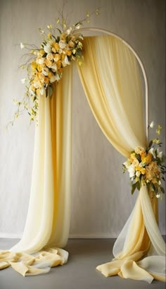 a yellow and white wedding arch with flowers on the top, draped over by drapes