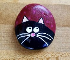 a painted rock with a black cat on it's face sitting on a wooden surface