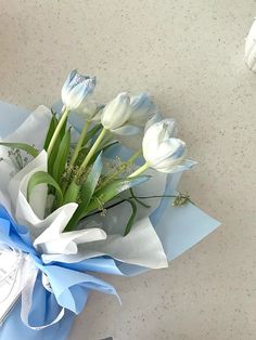 a bouquet of white tulips wrapped in blue paper on a counter top next to a pair of scissors