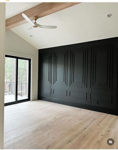 an empty room with black walls and wood flooring in the foreground is a ceiling fan