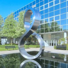 a large metal sculpture in front of a building with a bench and water feature next to it