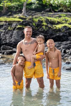 a man standing in the water with two children and an adult next to him wearing yellow shorts